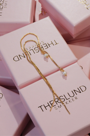 Therslund Smykker – Laura øreringe Laura kædeøreringene er ca. 16 cm lange og fremstillet i forgyldt messing. Disse elegante, guldfarvede øreringe afsluttes med en fin perle, der giver et feminint og let udtryk. Ørekæderne falder smukt og tilfører et romantisk og sødt touch til dit look. De er den perfekte gaveidé eller en stilfuld detalje, der kan løfte ethvert outfit og tilføje et strejf af elegance. Moderne og minimalistiske – ideelle til bryllupper, date nights eller når du ønsker at sætte lidt ekstra glans på hverdagen. Alle vores smykker er nikkel- og blyfri og overholder dansk lovgivning. Smykkerne er fremstillet i messing eller rustfrit stål og kombineres ofte med glasperler eller halvædelsten for at skabe unikke og holdbare designs.