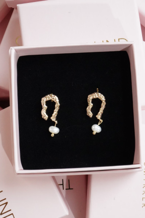 Therslund Smykker – Oliwia Ørestikker Olivia ørestikkerne er fremstillet i forgyldt messing og har et elegant, buet design, der leder tankerne hen på en hestesko eller en bølge. Designet fuldendes af en lille, hvid perle, der hænger diskret nederst på hver ørestik og tilføjer et tidløst og sofistikeret udtryk. Disse ørestikker er en ideel gaveidé eller en stilfuld detalje, der kan løfte ethvert outfit og tilføje et strejf af elegance. Alle vores smykker er nikkel- og blyfri og lever op til dansk lovgivning. Smykkerne er fremstillet i messing eller rustfrit stål og kombineres ofte med glasperler eller halvædelsten for at skabe unikke og holdbare designs.