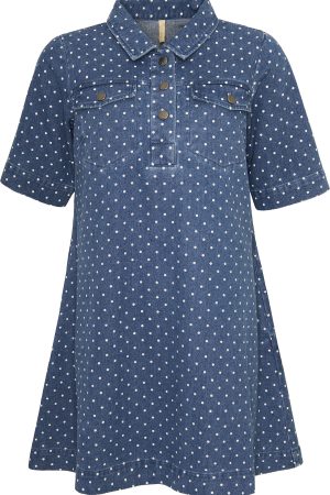 Ofelia Kjole Dana Tunic Blue Den her kjole/tunika er en afslappet og stilfuld hverdagsfavorit med et klassisk twist. Den er lavet i denim-look stof i en blå nuance og har et fint prikket mønster, som giver et let og legende udtryk. Designet skjorte krave og en kort knaplukning foran, hvilket giver et casual, men stadig velklædt look. Pasformen er løs og behagelig – næsten A-formet – så den falder flot og giver god bevægelsesfrihed. De korte ærmer gør den perfekt til varmere dage, eller du kan style den med en langærmet bluse under, når det er køligere. De små brystlommer med knapper tilføjer en praktisk og dekorativ detalje, som understreger det afslappede denim-inspirerede design.