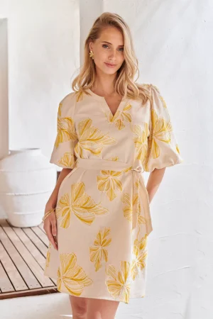 Smashed Lemon Kjole 26051 Leder du efter den perfekte kjole til en havefest eller en solskinsdag i byen? Denne kjole fra Smashed Lemon kombinerer elegance med ren komfort. Kjolen har den samme smukke beige base og gyldengule blomsterprint, og er fremstillet i en flatterende A-formet stil. Med det matchende bindebælte kan du nemt fremhæve din talje for en feminin silhuet. Smashed Lemon-kjolen har en diskret halsudskæring og halvlange pufærmer med elastik, der giver ensemblet et romantisk og tidløst look. Bær den med et par smukke sandaler eller hæle for et komplet look.  Smuk A-formet kjole med gyldengult blomstermotiv. Inkluderer matchende bindebælte for en fremhævet talje. Fremstillet med Smashed Lemons signaturkvalitet
