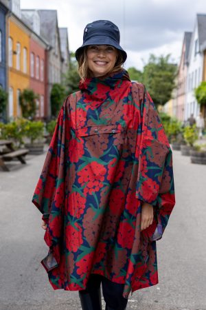 Danefæ Danepackit Rainponcho Maxiberry Super smart regnponcho med hætte, der kan snøres ind, og er med funktionel lomme foran, som regnponchoen kan foldes sammen i. Når ponchoen er foldet sammen, kan den helt nemt medbringes på de dage, hvor vejret kan vvære ustabilt. Lommen på forsiden har et lille logo af en fin svane, som også kommer til syne, når ponchoen er foldet sammen. Regnponchoen har et fint mønster med røde og brune bær og et rummeligt design. Den fås i flere varianter med smukke mønstre. Den sammenfoldede poncho måler: 21 x 24 cm.